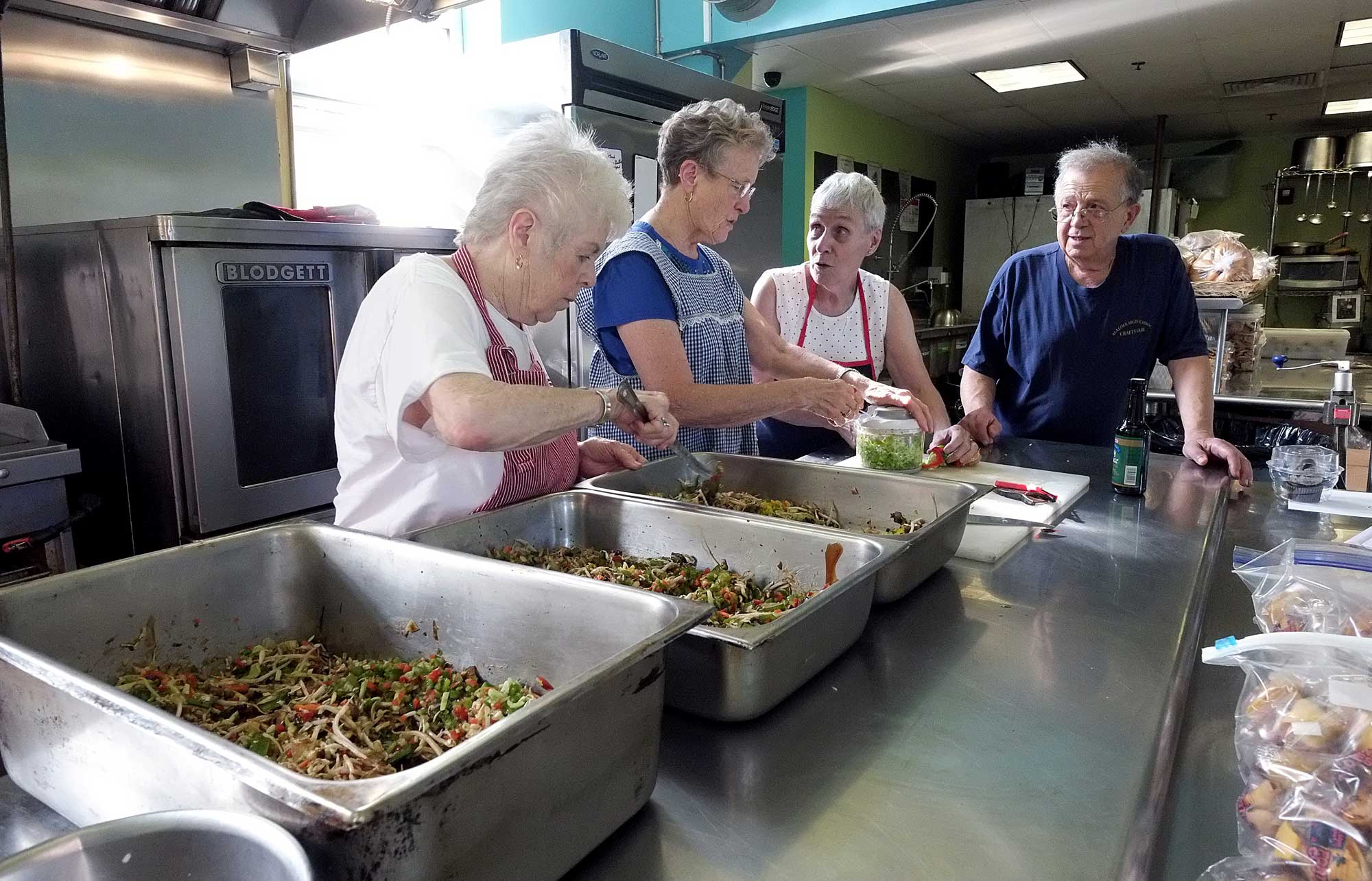 Three women in aprons and one man prepare a community meal.