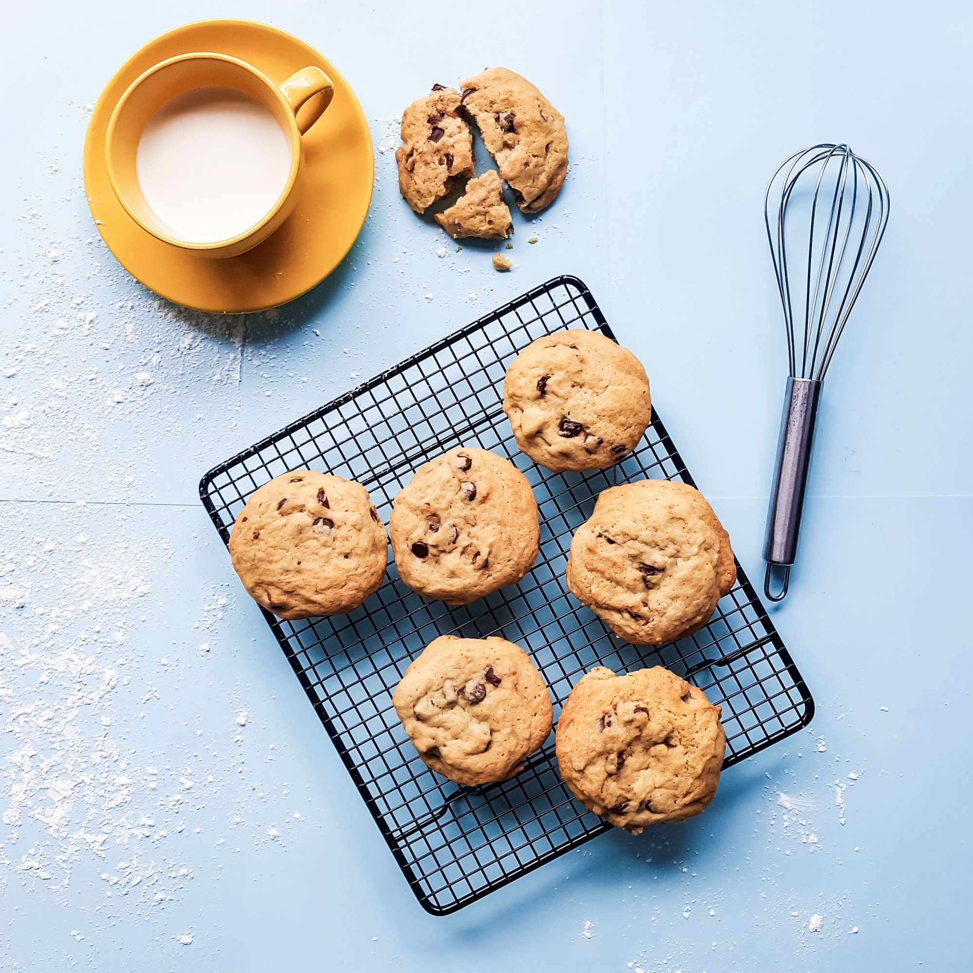 A photograph of cookies on a cooling rack next to a mug of milk.