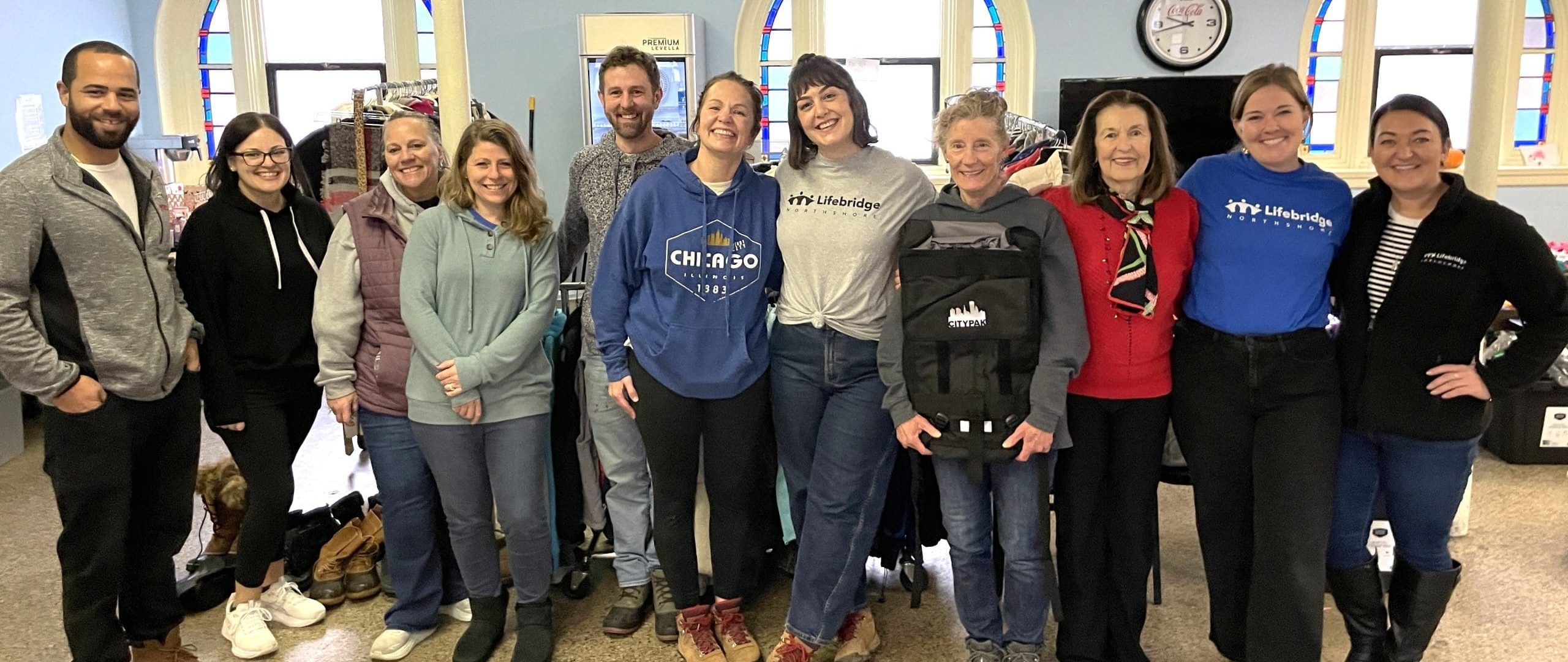 Eleven Lifebridge volunteers and staff members pose with a City Pack backpack for a group photo.