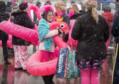 Woman in a flamingo floaty with small crowd of people in flamingo floaties in the background, with snow falling around them.