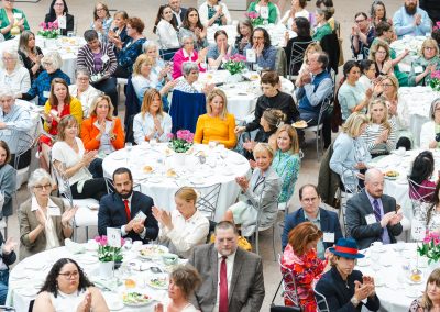 An overhead view of people sitting at round tables clapping their hands.