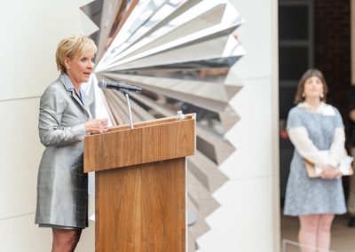A woman is speaking at a podium with a second woman in the background holding a clipboard.