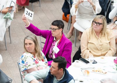 Woman in violet blazer making a bid at event