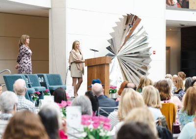 Woman standing and speaking at a podium. A second woman stands next to and slightly behind her.
