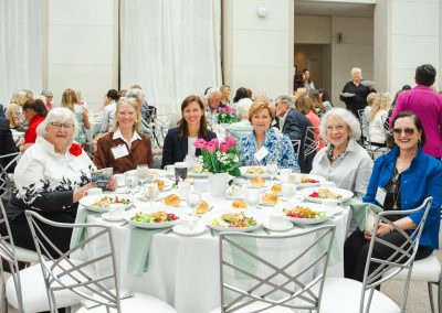 Six women are sitting around a table, smiling, with food in front of them.