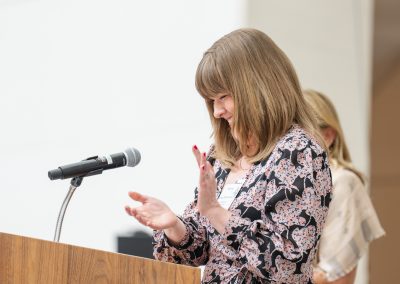 This seventh photograph shifts perspective from the audience to the stage of the same formal charity event, focusing on a speaker at the podium.