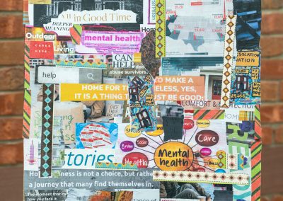 The photograph shows a square mixed-media art collage displayed on a black metal easel stand. The collage is composed of various cut-out magazine clippings, text fragments, maps, newspaper sections, and colorful patterned paper strips glued together to explore themes related to home, homelessness, and mental health.