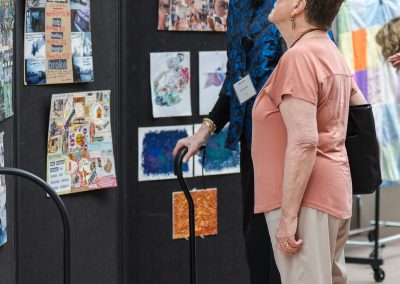 The image shows a candid indoor photograph of two senior women looking at an art exhibition or project display.