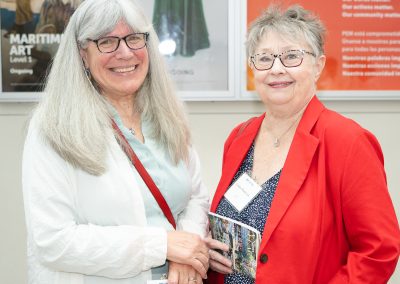 The image shows a candid indoor photograph of two smiling, adult women standing side-by-side.