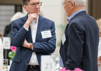 The image shows a candid indoor photograph of two senior men engaged in conversation during an organized luncheon or reception.