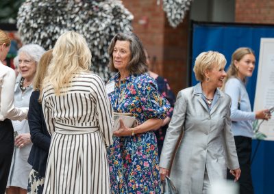 The image shows a candid indoor photograph capturing a large group of well-dressed attendees socializing at a bustling reception or event.