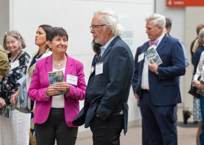 The photograph captures a candid moment during a well-attended reception or community gathering, focusing on a man and woman engaged in conversation while other guests mingle nearby.