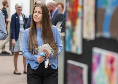 The photograph captures a candid moment of a young woman walking through a bright, open art exhibition space or community event.