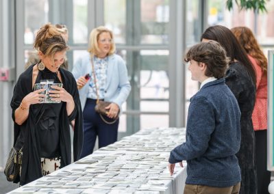 The photograph captures a lively check-in or registration area at an indoor event, featuring a long table filled with rows of name tags.