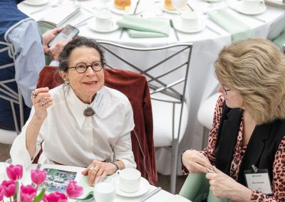 The photograph captures an overhead, candid view of two women engaged in conversation while seated at a dining table during a formal luncheon or banquet event.