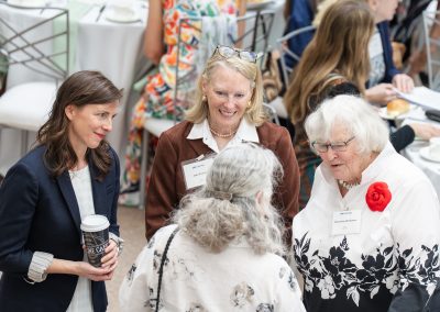 The photograph captures an overhead, candid moment of four women engaged in a friendly conversation during an organized indoor luncheon or reception.