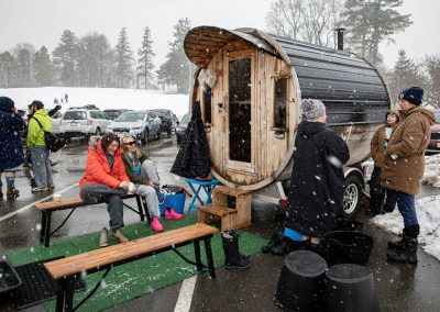 Mobile wood sauna, with people sitting on benches preparing to go into the sauna.
