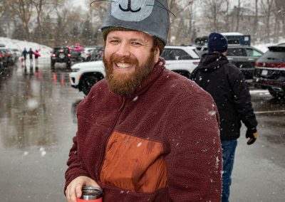Man with a seal hat holding a thermos, smiling at the camera.