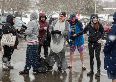 Participants of the polar plunge standing in the parking lot, participant in the middle is wearing a seal onesie.