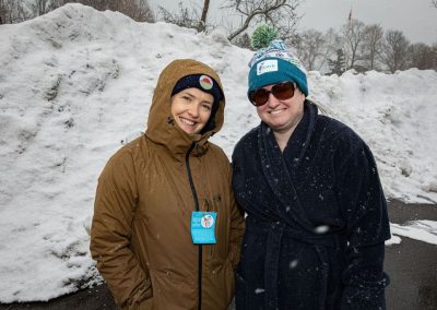 Two woman standing in the snow smiling at the camera.