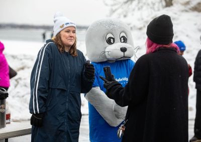 Lifebridge employee and Shoebert seal mascot talking to a woman in a jacket and beanie.