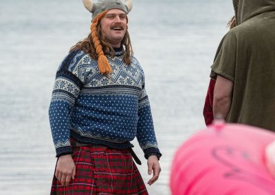 Man standing on the beach in a kilt, sweater, and viking braid beanie.