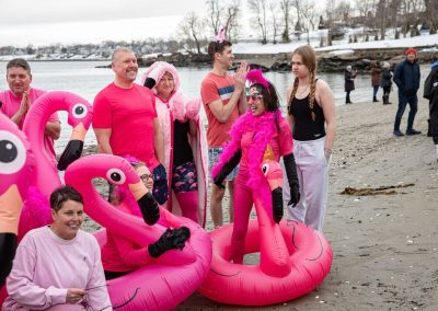 Plunging group sitting and standing on the shore post plunge with their pink flamingo floaties.